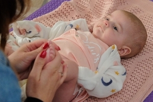 A baby laying on a mat having their foot massaged at one of our Family Hub baby massage sessions.