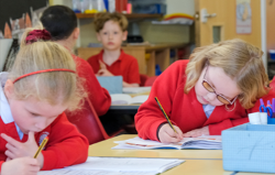 Primary school children sat at a desk focusing on school work.