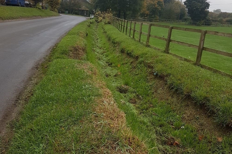 A ditch in a grass verge alongside a rural road.