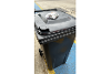 A black rubbish bin with a clear bag of batteries on top.